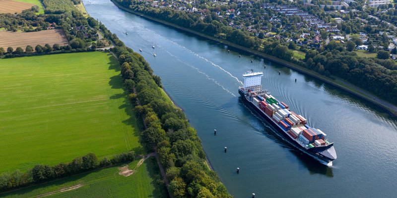 Foto zeigt Containerschiff auf Fluss. Link führt zu KuWiK-Portal.