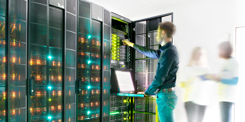 Foto zeigt einen Mann der im Serverraum steht und Server über ein Notebook steuert. Link führt zum IT-Navigator